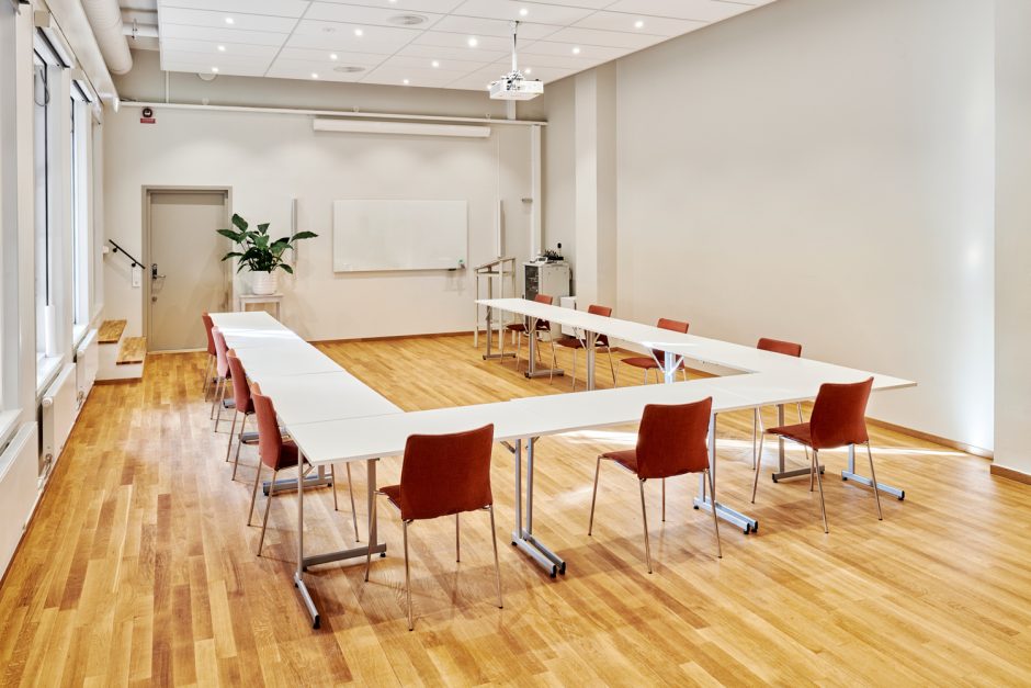 Ett rum med whiteboardtavla och bord som står i en halv fyrkant med tillhörande stolar
