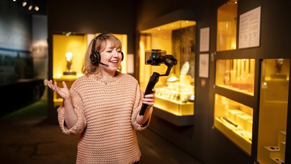 Kvinna med hörlurar håller och tittar in i en mobiltelefon och ler