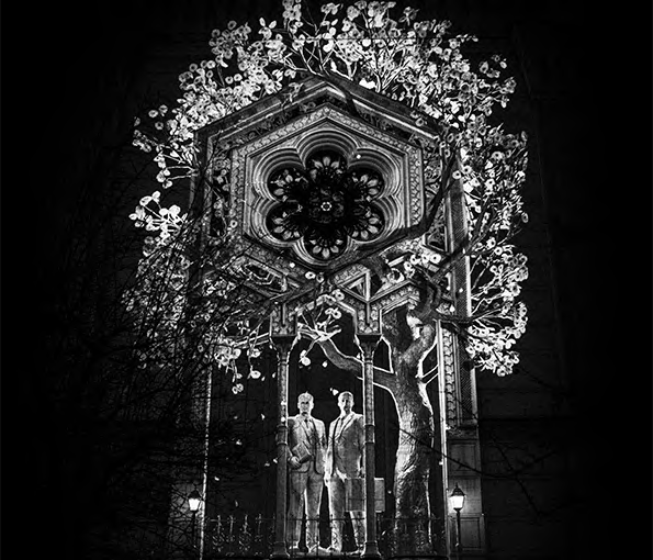 Black and white projection of two men standing under trees.