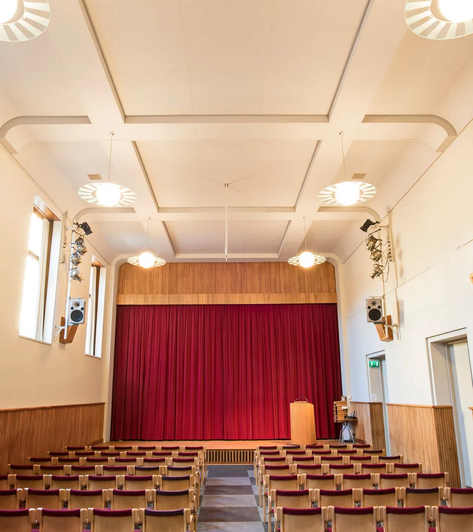 Scen längst fram med ett rött draperi. Rader med stolar framför.
