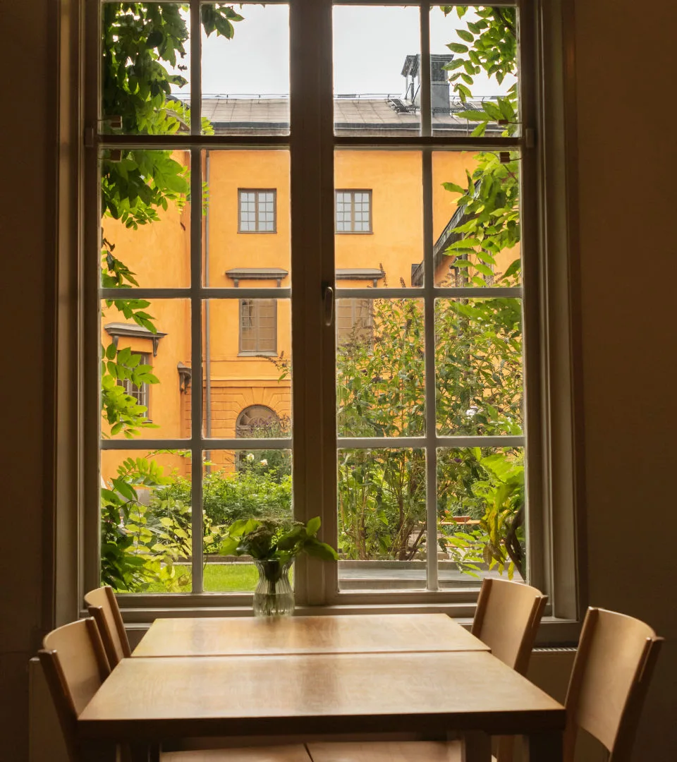 Ett bord med fyra stolar står framför ett stort fönster. Gröna träd utanför.