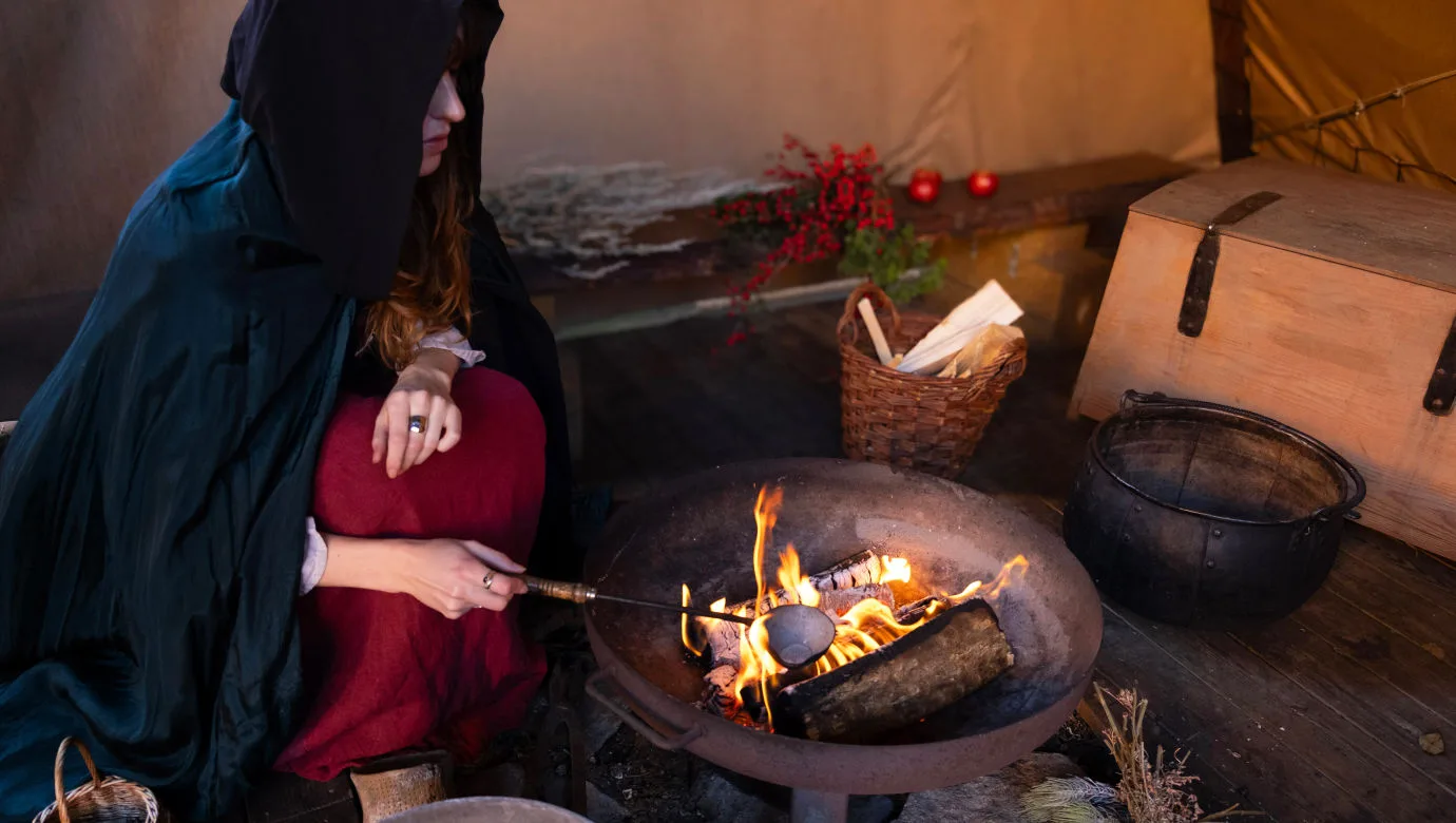 En person sitter med en mörk mantal framför en brasa.