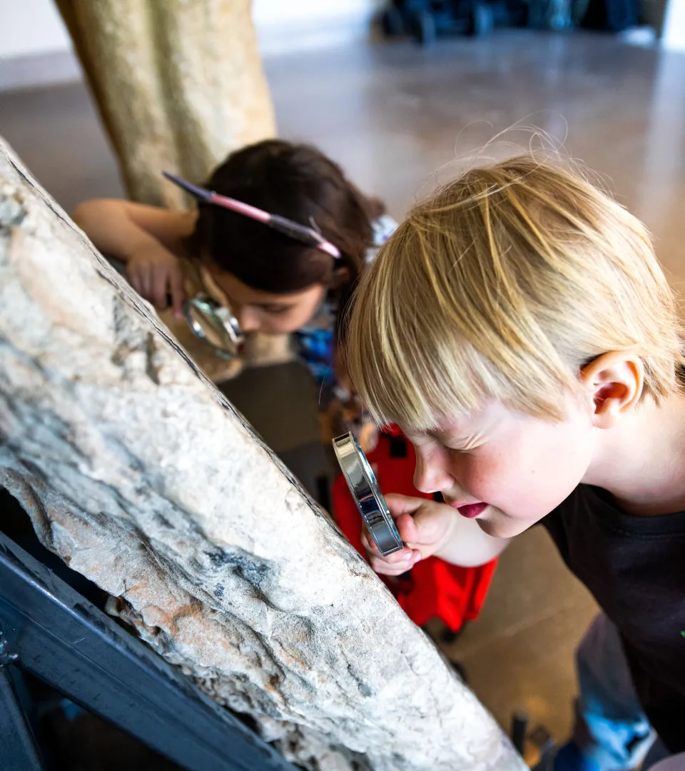 Två barn undersöker en runtsten med varsitt förstoringsglas.