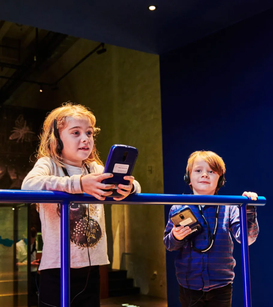 Two children, each with an audio guide, in an exhibition.