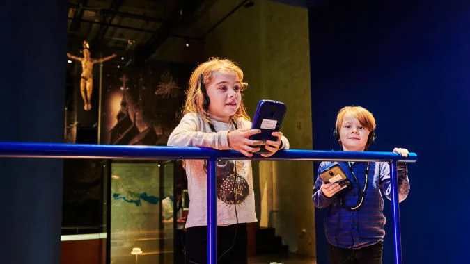 Två barn med varsin audioguide i en utställning.