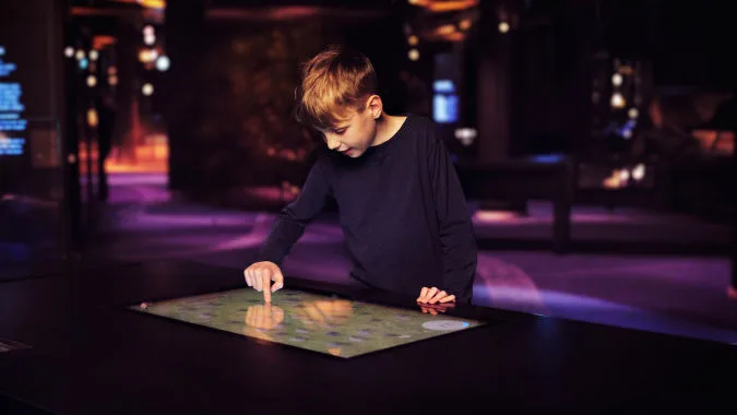 Barn använder en digital pekskärm i utställningen Vikingarnas värld.