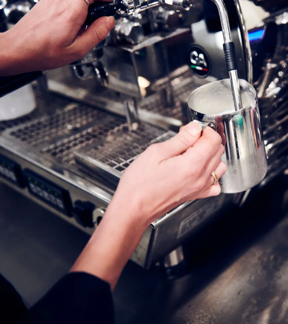 En person skummar mjölk i en kaffemaskin.