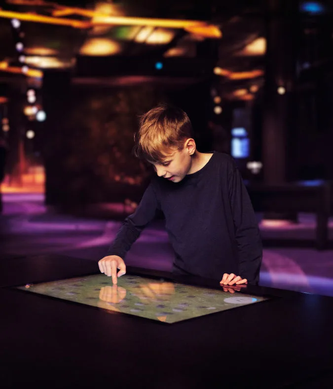 Barn testar en digital pekskärm i utställningen Vikingarnas värld.