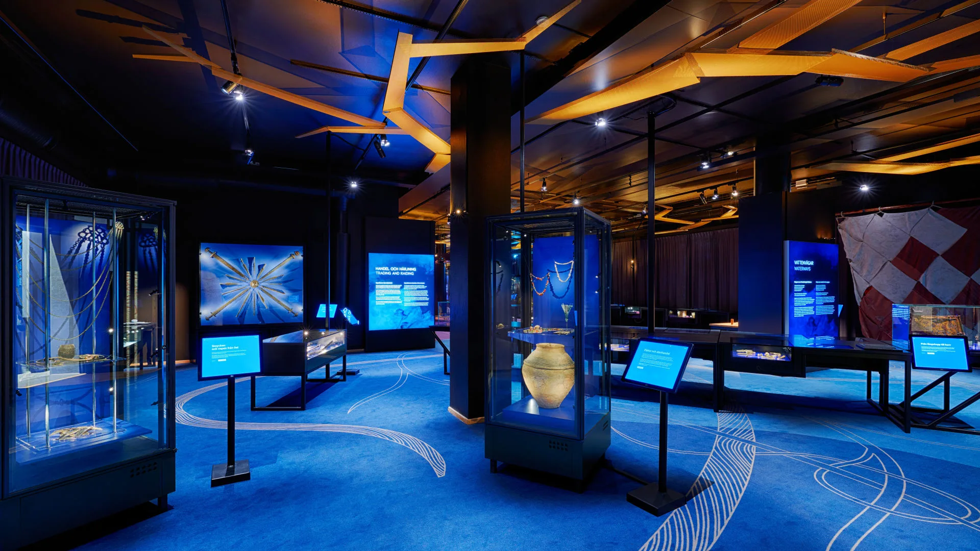Exhibition room with many objects, info screens, and blue carpet