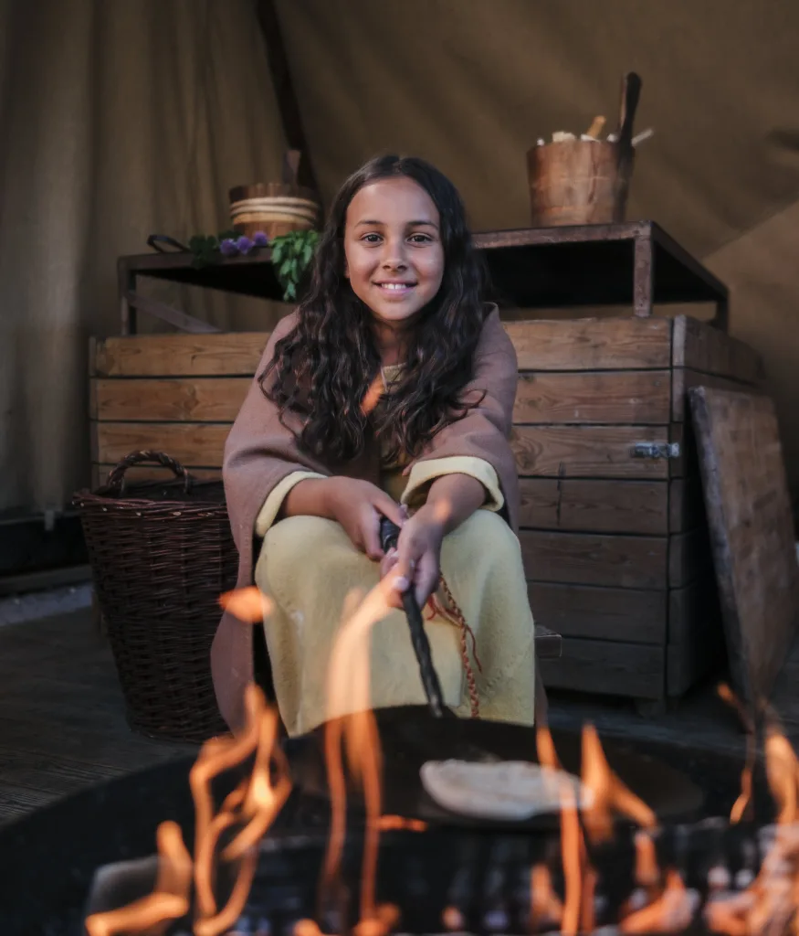 Ett barn bakar bröd över öppen eld.