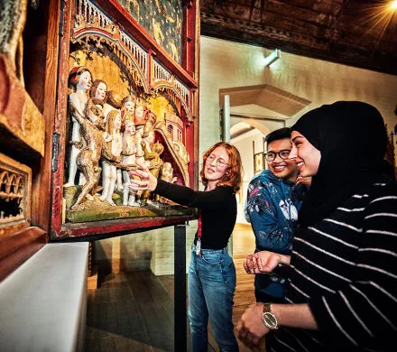 Pedagog håller i en visning. Två personer tittar på ett föremål.