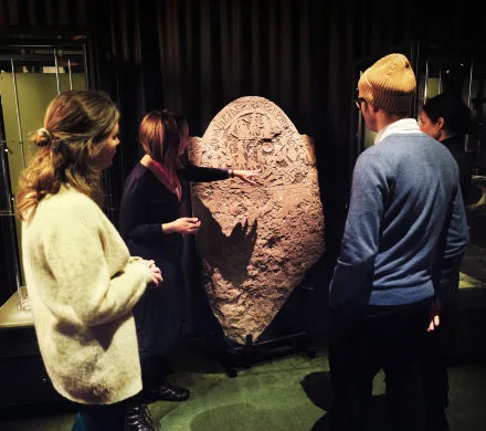 Pedagog visar en runsten för några besökare.