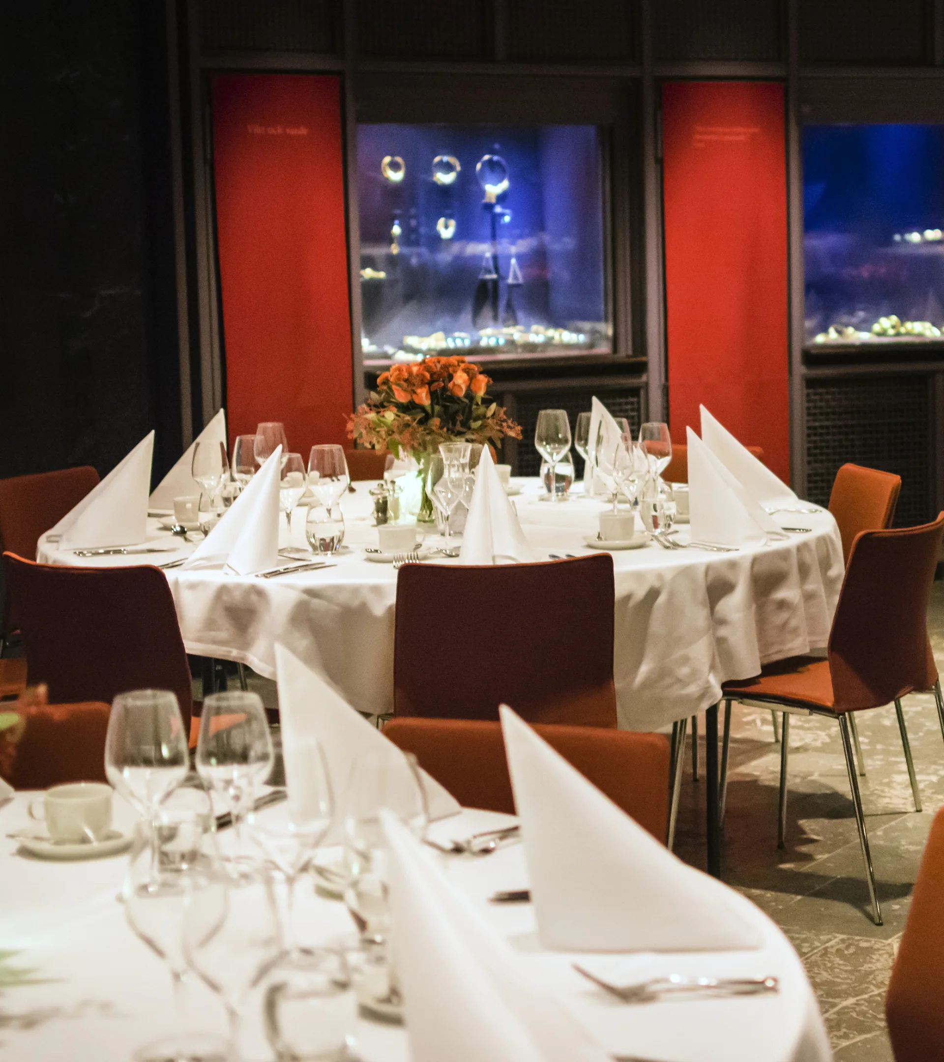 Runda bord med vita dukar, servetter och porslin på bordet. I bakgrunden syns montrar med föremål i museets Guldrum.