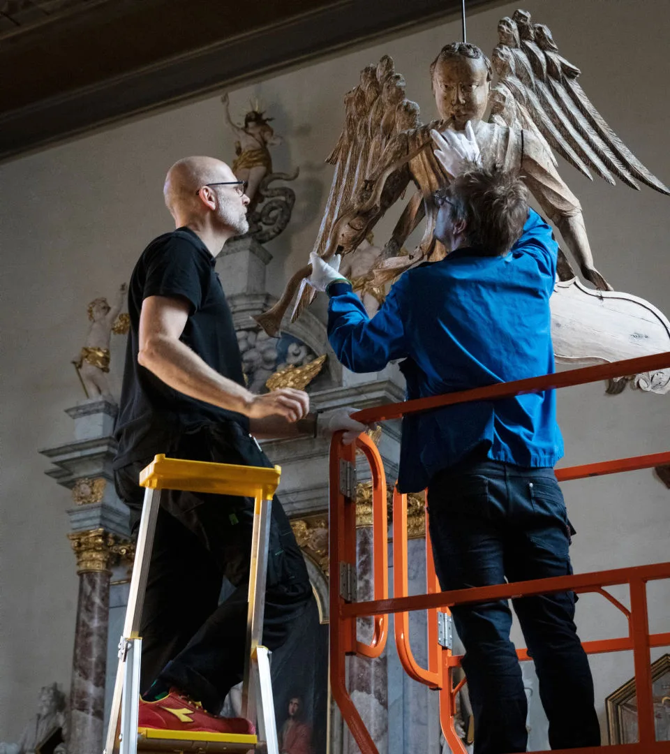 Two museum staff standing on a ladder working on an object.