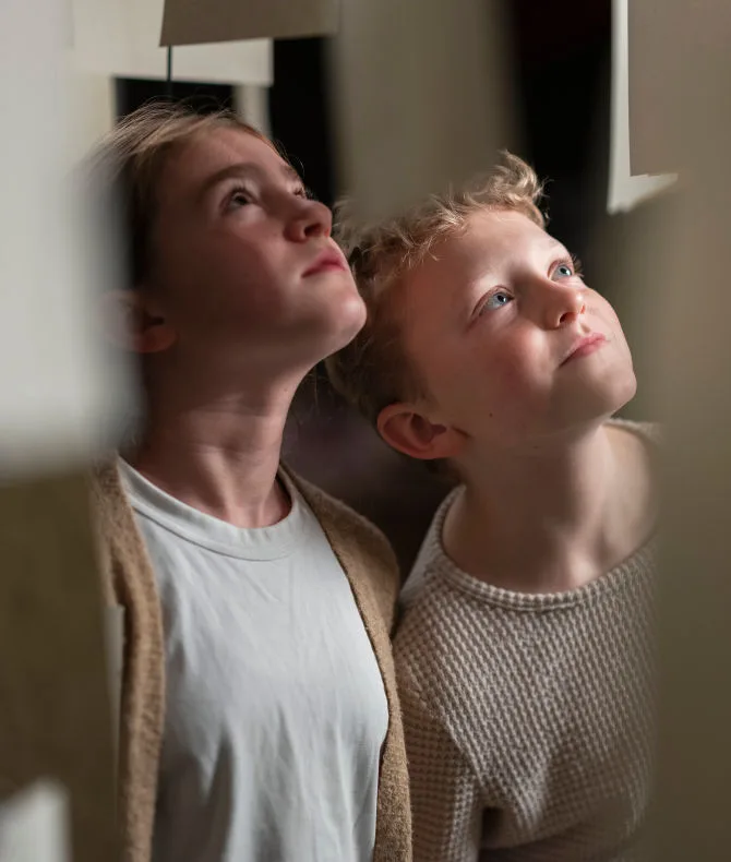 Två barn tittar upp mot teckningar på papper.