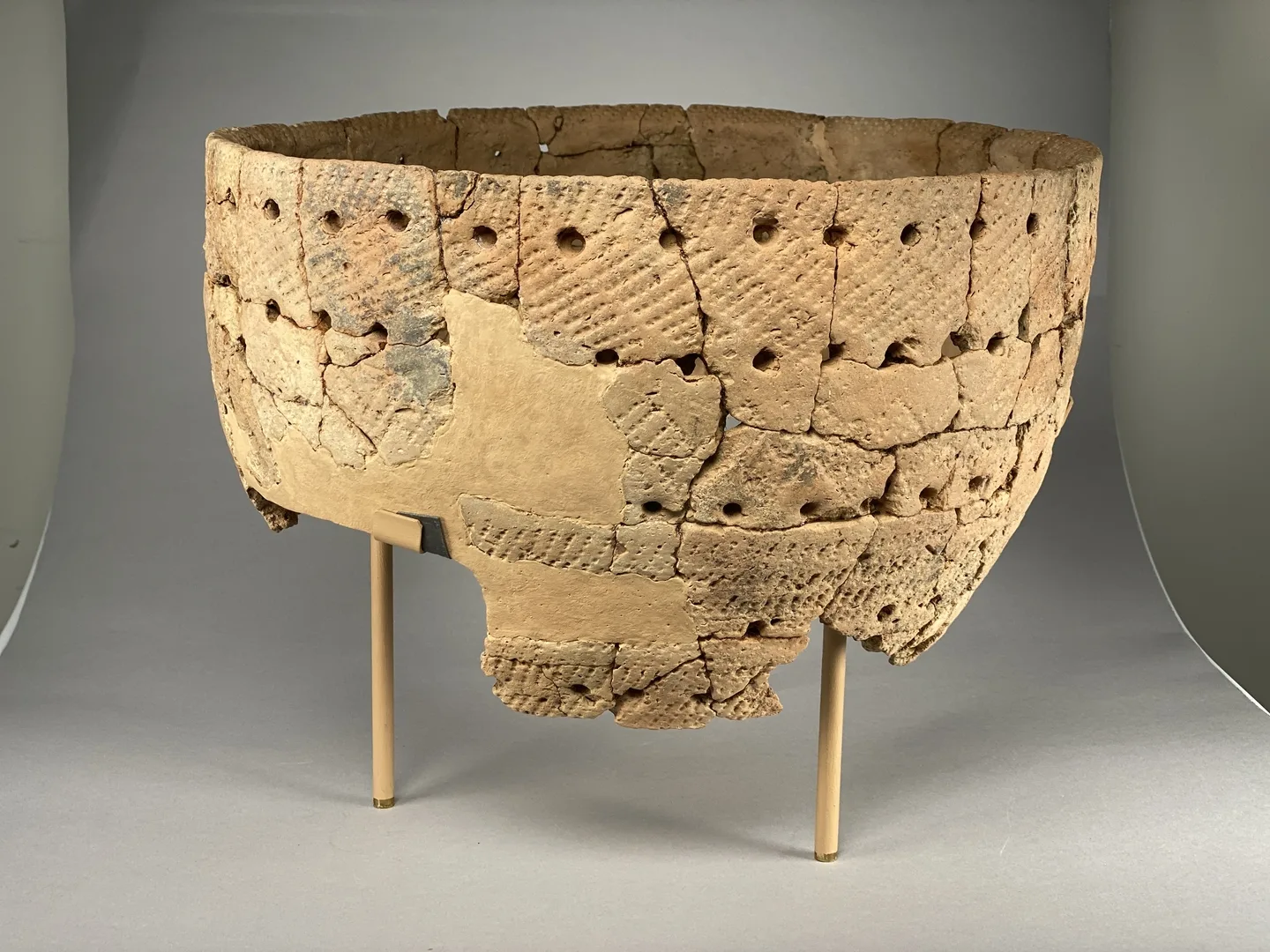 A broken clay vessel missing the bottom part. The vessel has a lot of perforations.