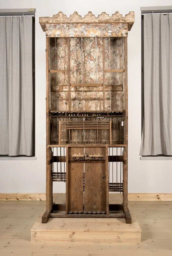 A wooden organ resembling a cabinet with wires and supports.
