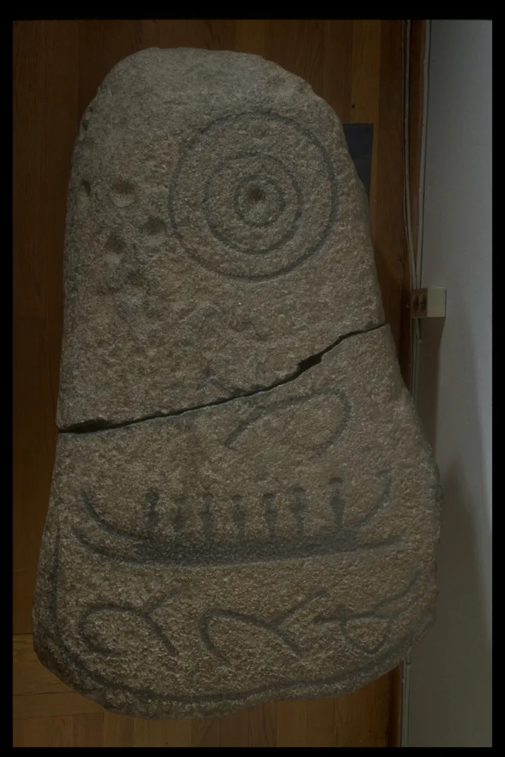 An elongated stone with round ends, decorated with circles, squiggles and a ship.