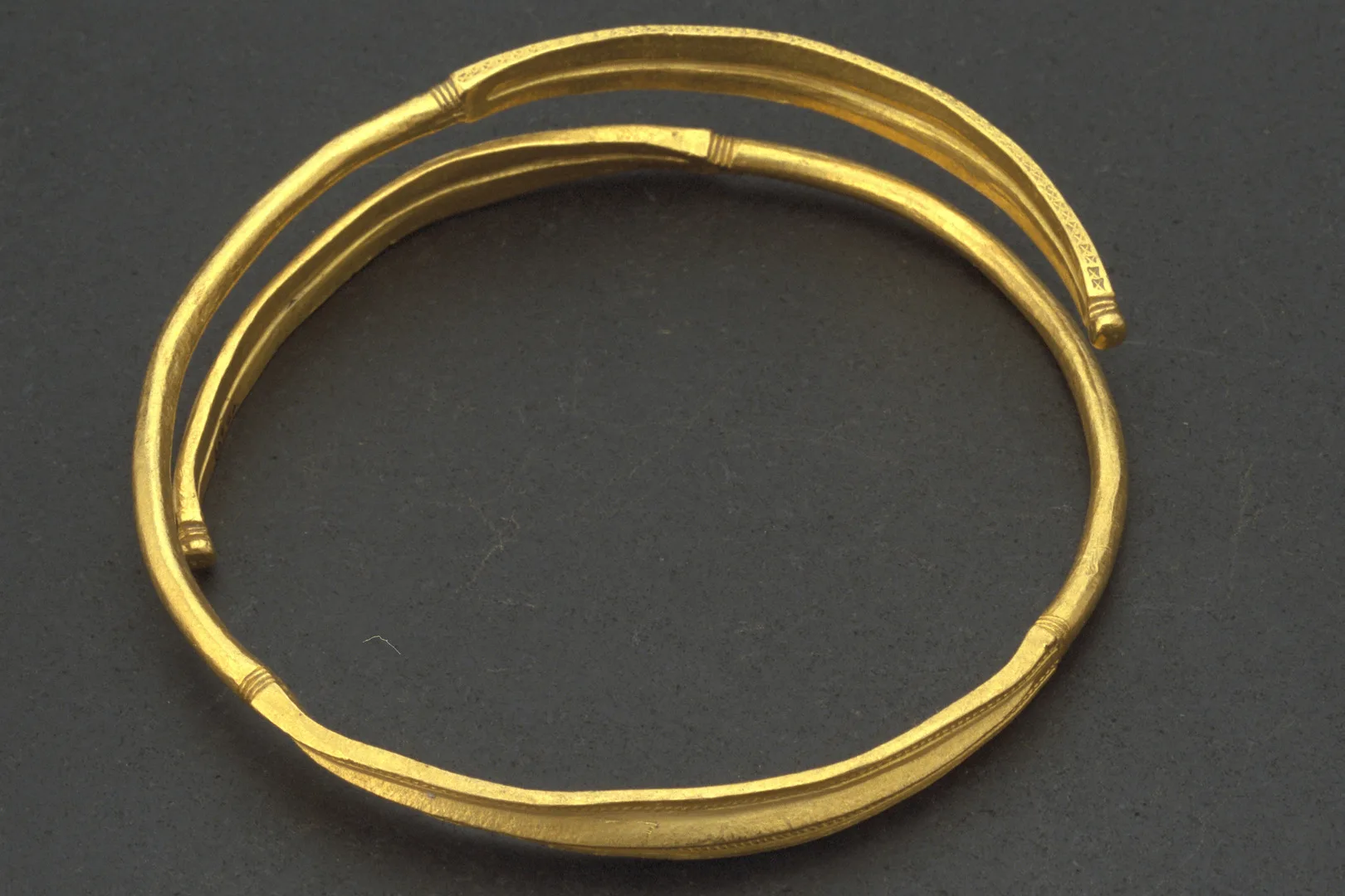Armring av guld som är böjd ett och ett halvt varv. Mitten av ringen är profilerad och ändarna avslutas med en liten rundel.