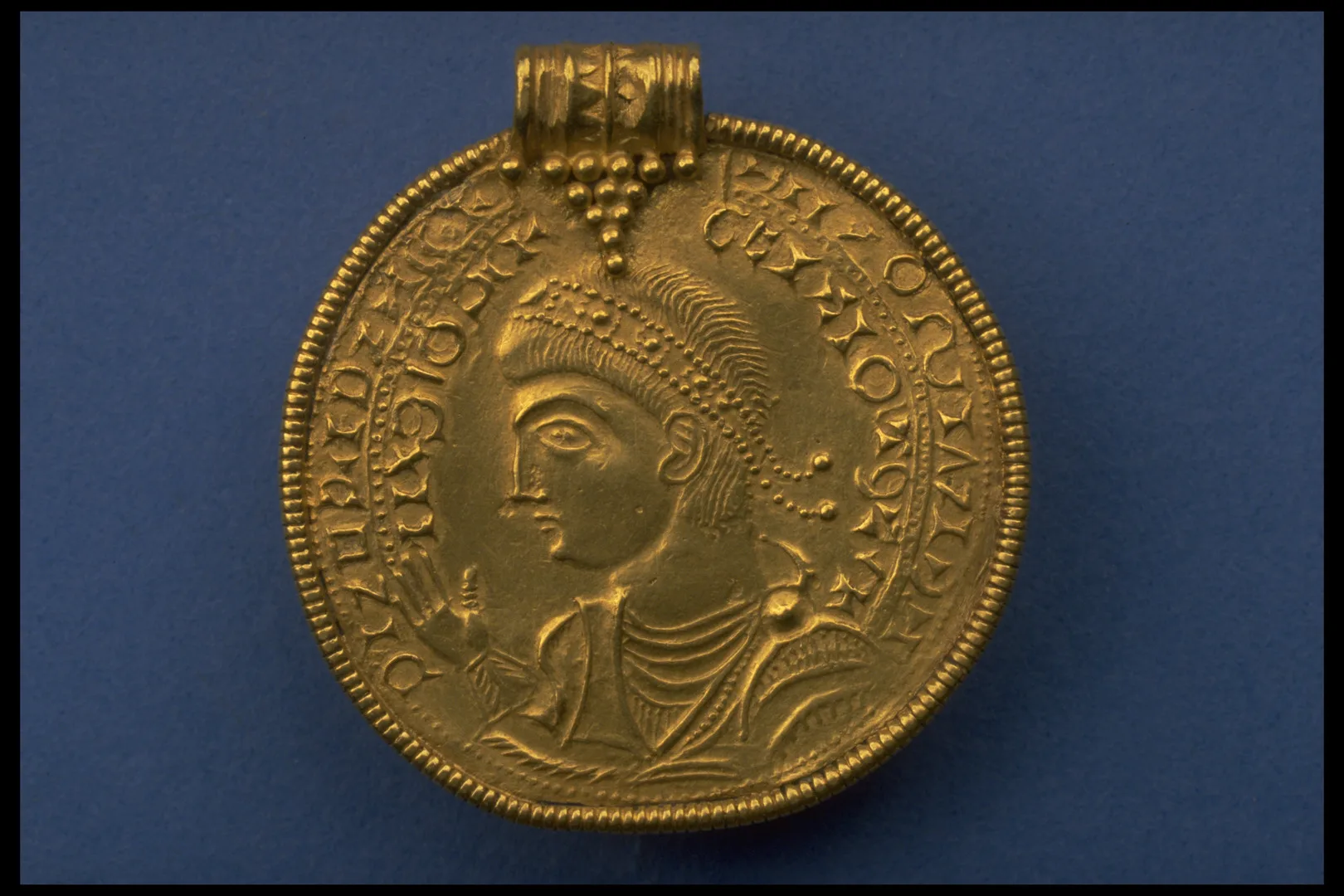 A gold medallion featuring a portrait. Around the portrait there are letters. 