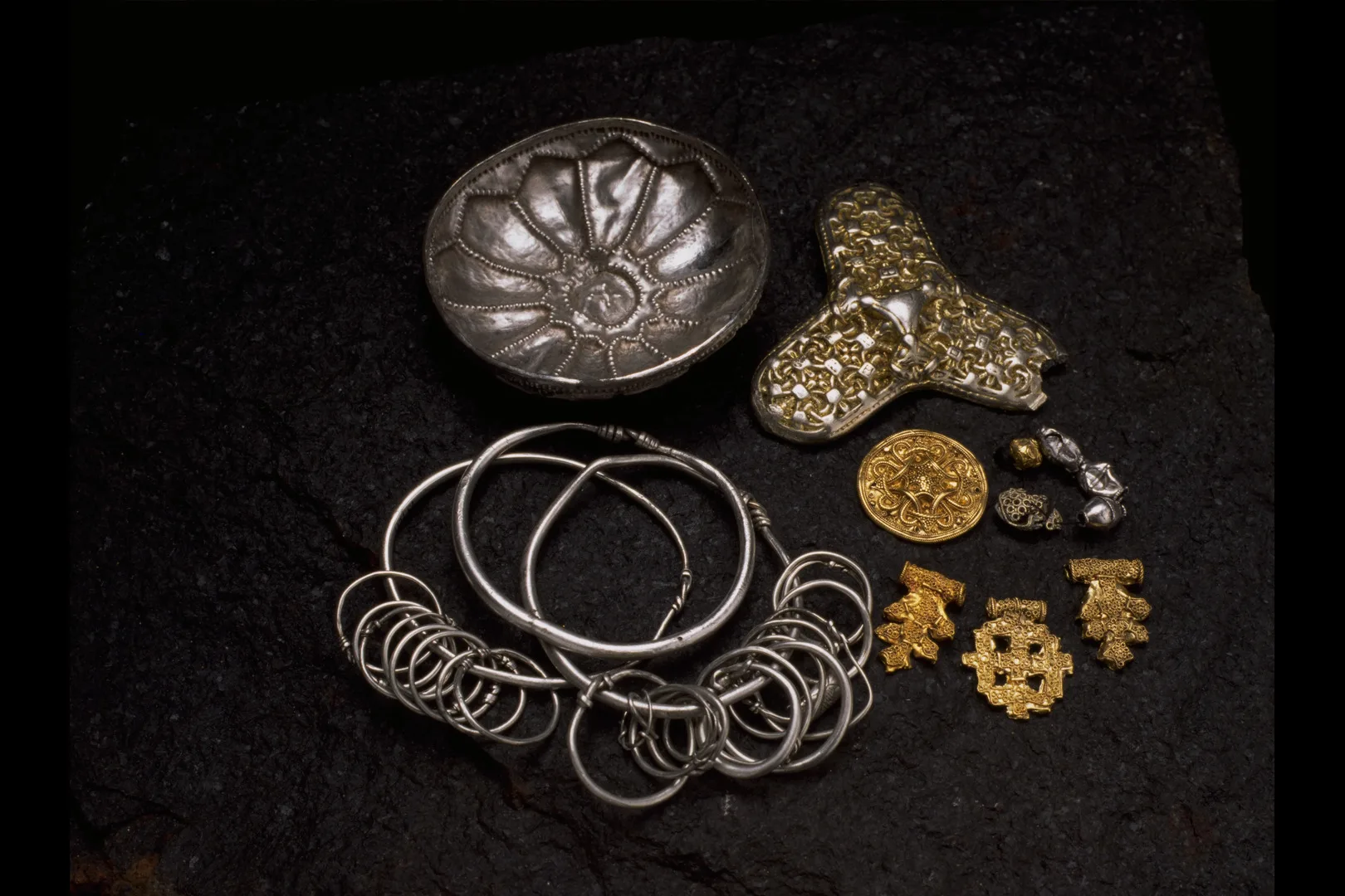 Föremål ur Lackalängaskatten ligger uppradade. Bland annat ett guldspänne och hängen.