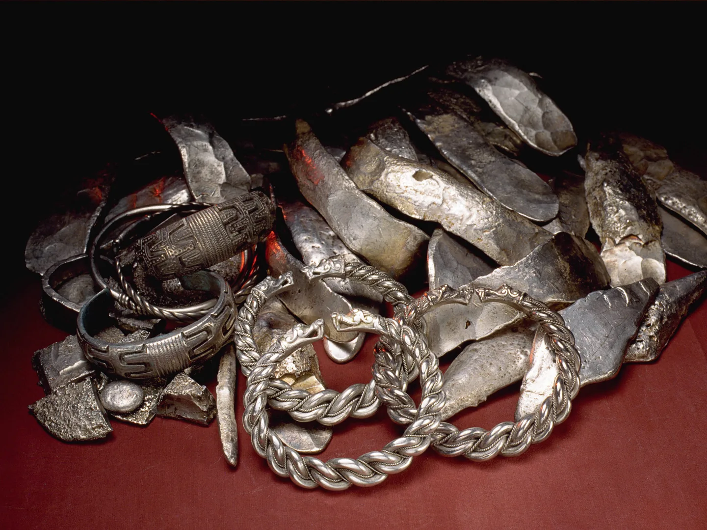 En hög med ringar, stenar och bitar av silver på en röd bakgrund.