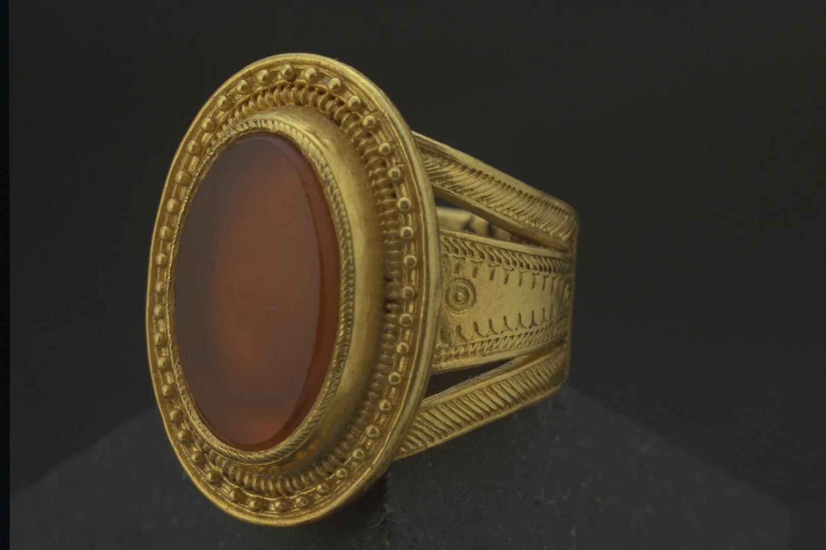 A large gold ring, consisting of three rings and an oval disc set with a red, flat stone.