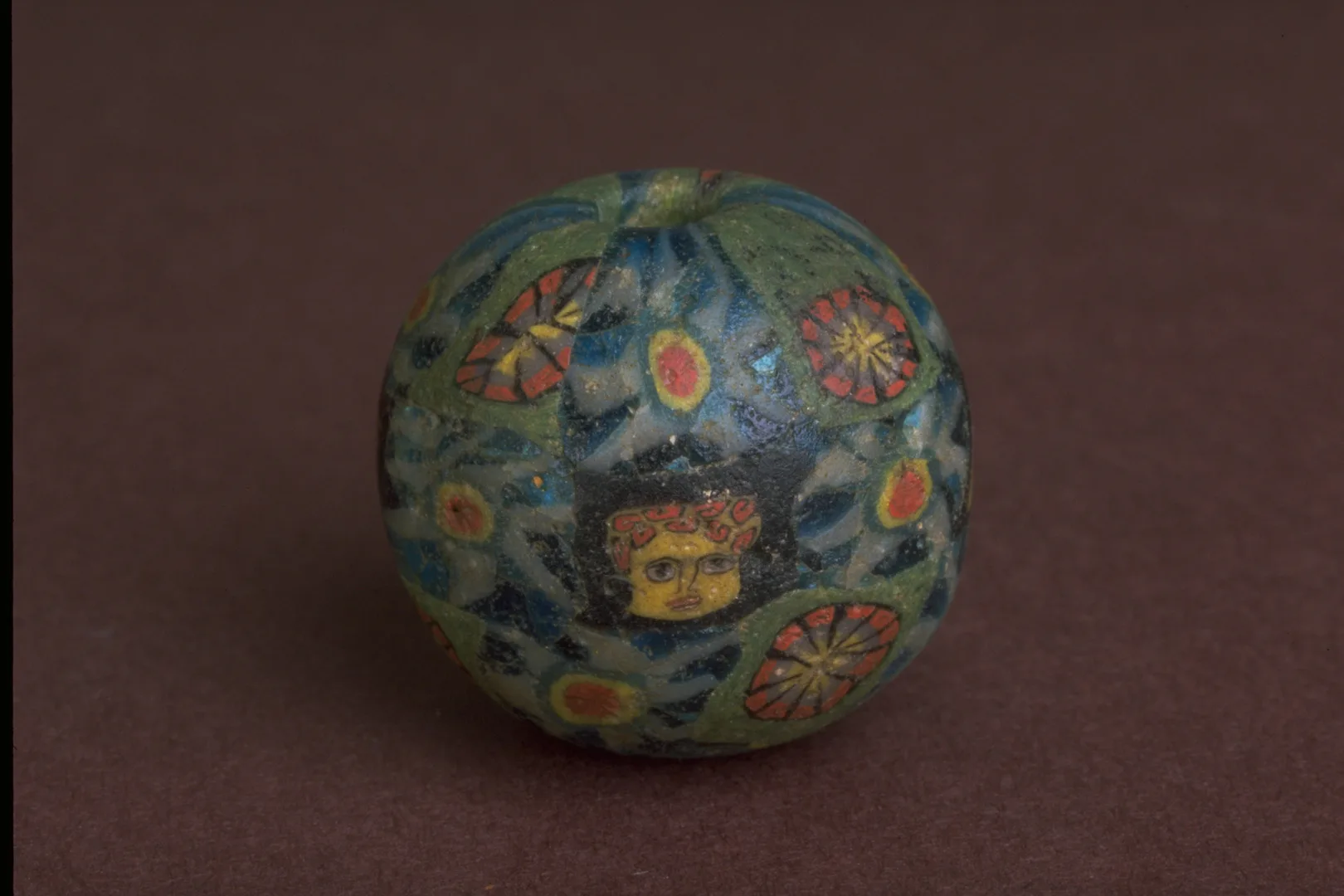 En rund kula med ytan täkt av färgglada blommor och ett gult ansikte.
