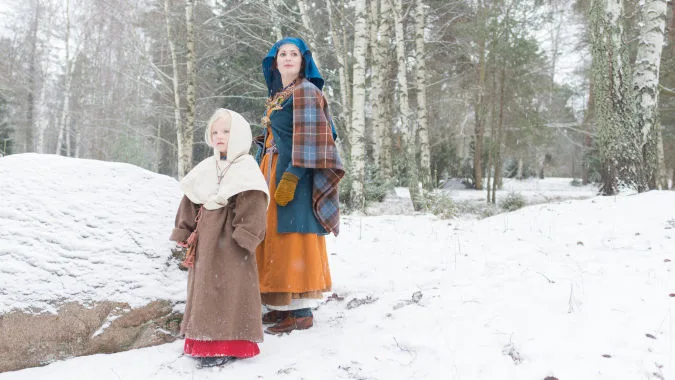 Adult and child in reconstructed Viking Age clothes stand in the snowy woods