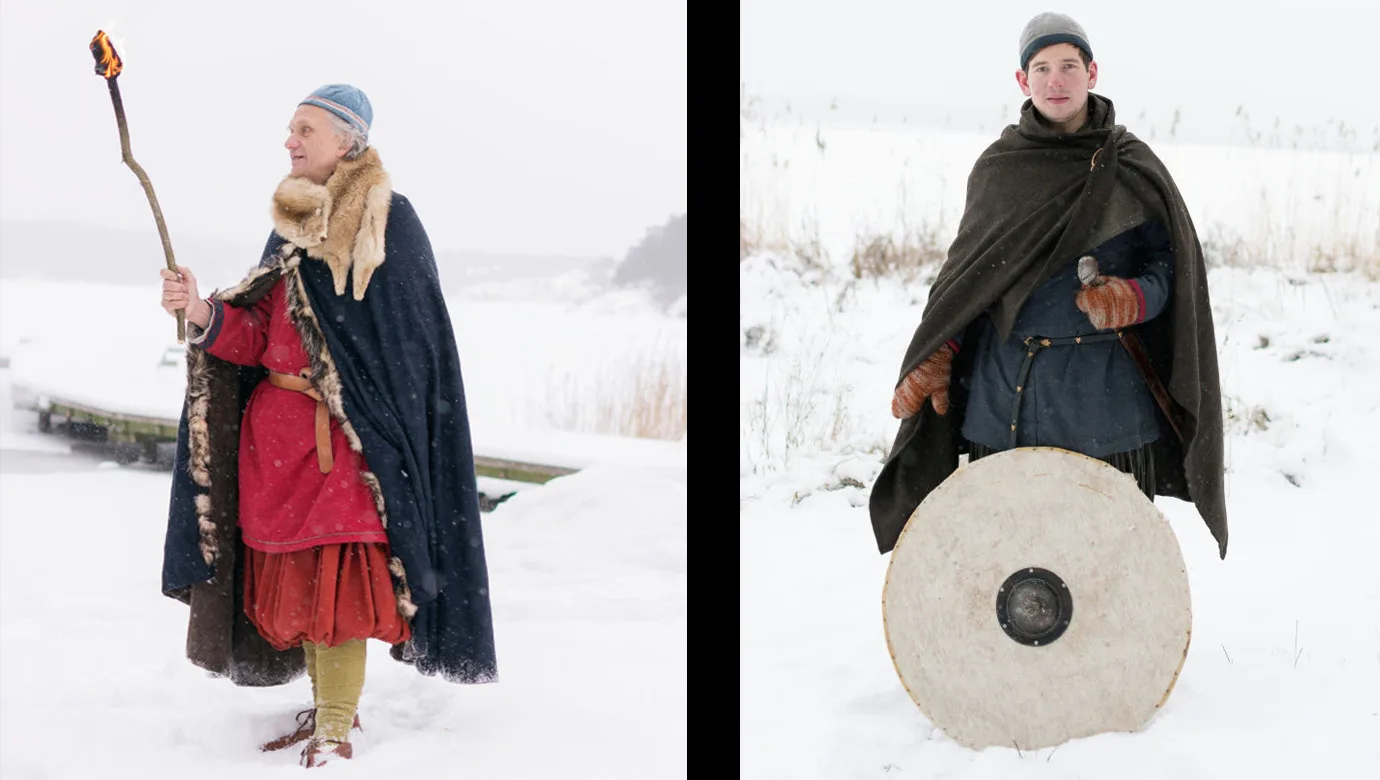 People in reconstructed Viking Age clothes. The man to the left has a torch and the man to the right holds a shield.