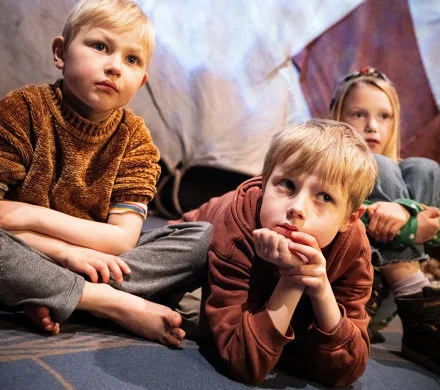 3 barn sitter på golvet och lyssnar.