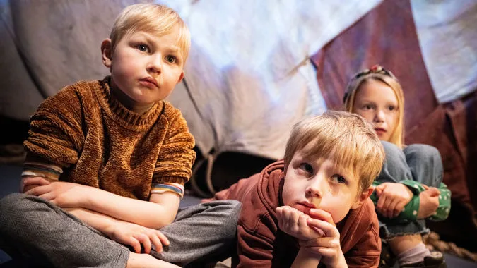 Tre barn sitter på en matta på golvet i museet.