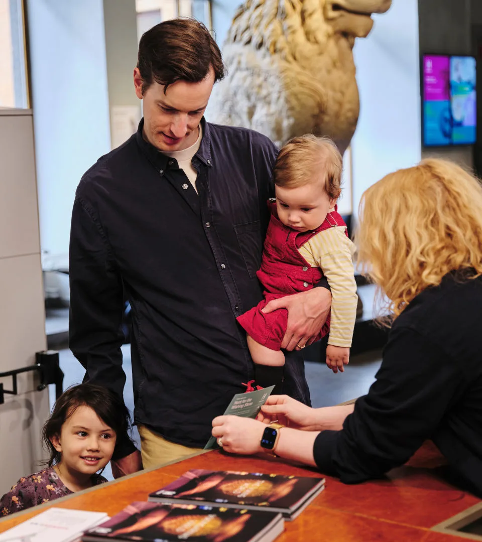 Barnfamilj står i kassan och får hjälp av en värd.