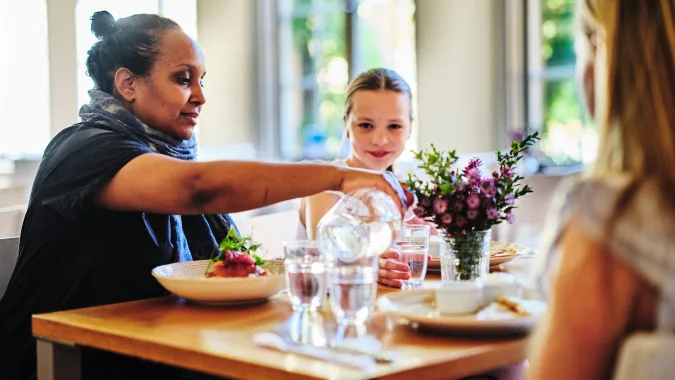 En person häller upp vatten i ett glas i restaurangen åt ett barn.