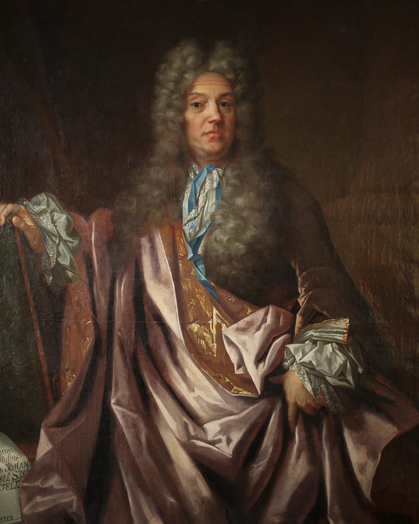 Ett porträtt föreställande en man med lång, lockig, grå peruk. Han är klädd i sidenkläder och har en stor , lila sidenmantel kring sig. Han stödjer sig mot en käpp och tittar högdraget på betraktaren.