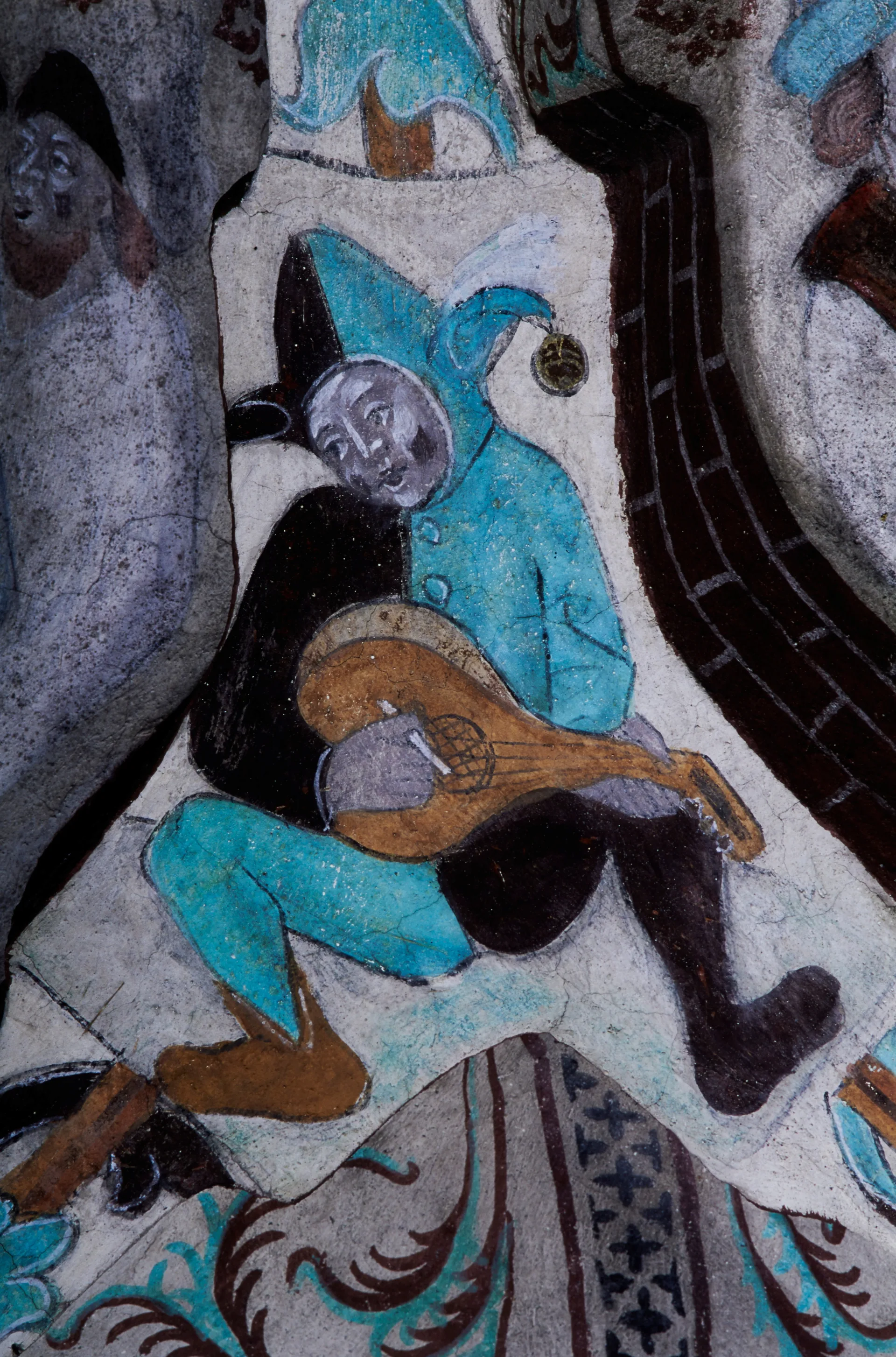 A man in a two-coloured onesie sitting and playing a lute.