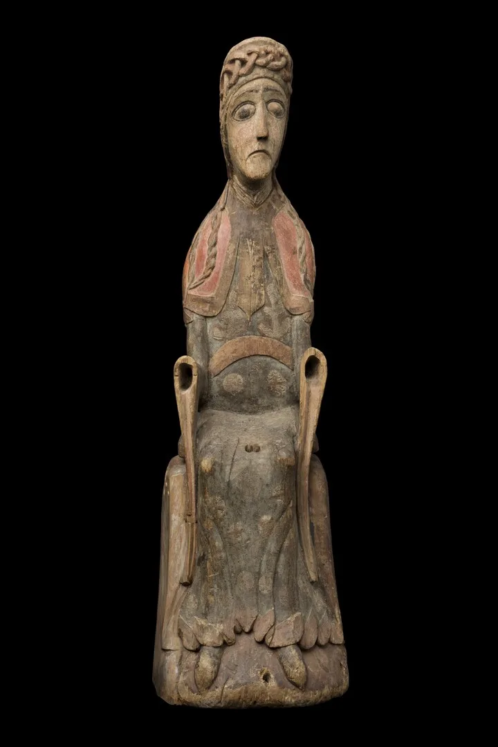 A wooden sculpture of a woman sitting. The sculpture's hands are missing.