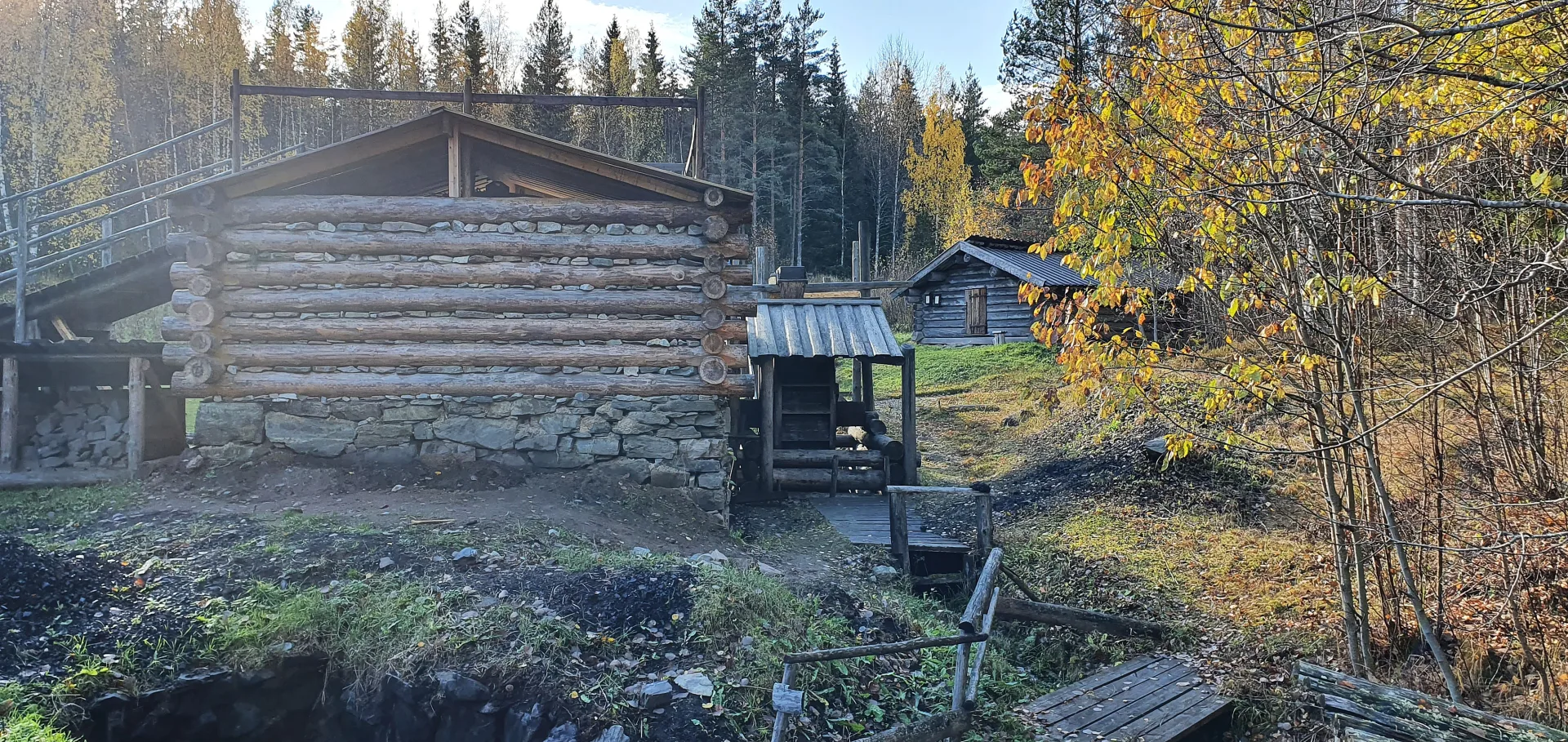 Wooden houses built with logs and stone in an autumn landscape.