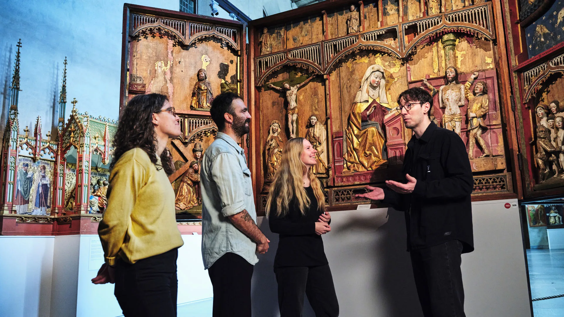Museum staff guiding visitors in front of a medieval alterpiece
