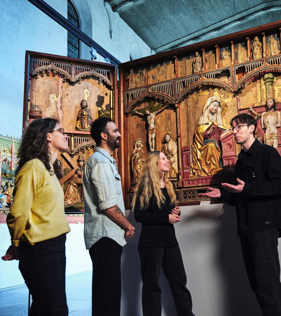 En pedagog står och pratar med besökare. Bakom syns en altartavla. Pedagogen gestikulerar med händerna.