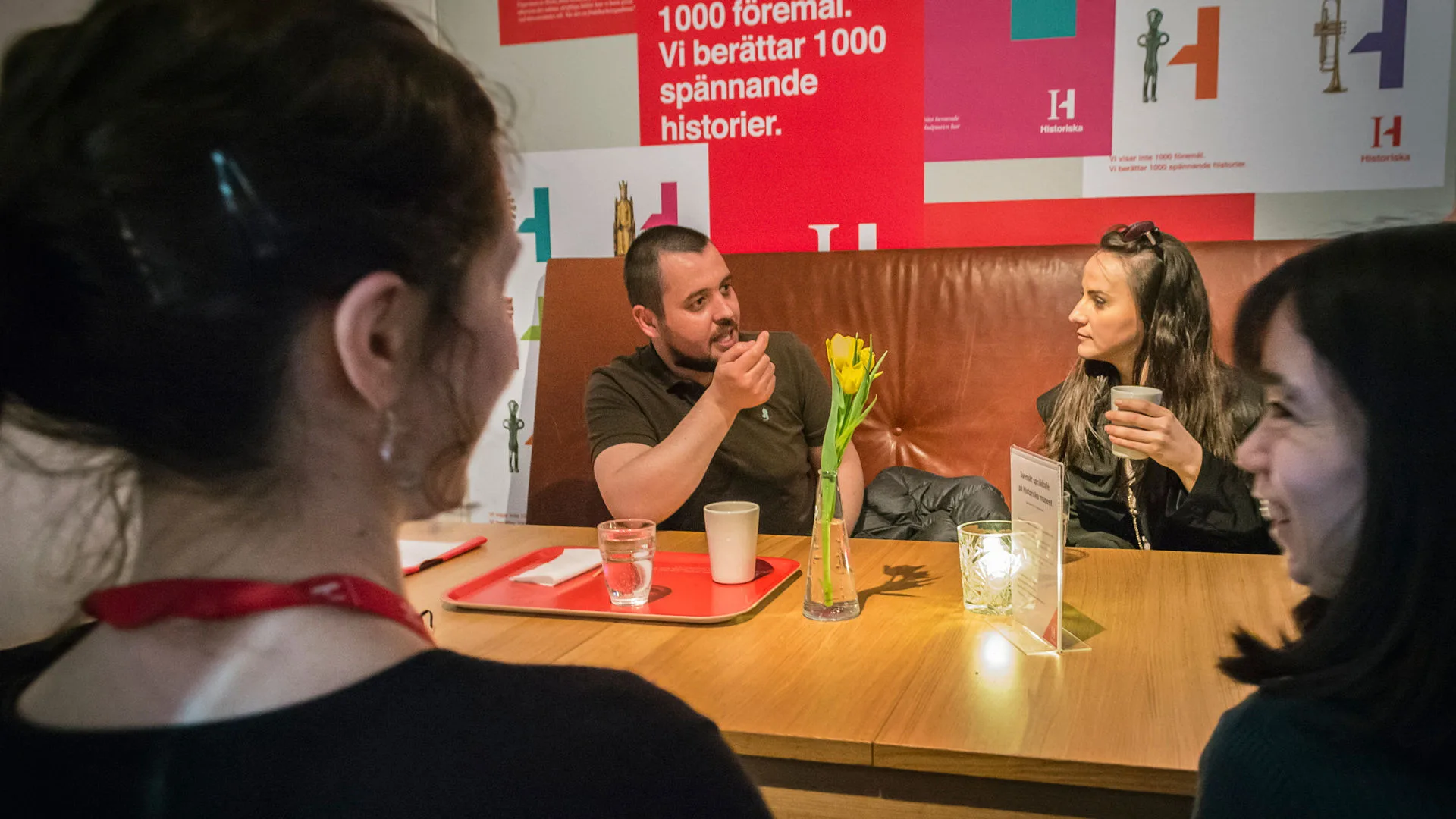 Personer sitter vid ett bord i museets restaurang och samtalar. De står kaffekoppar på bordet.