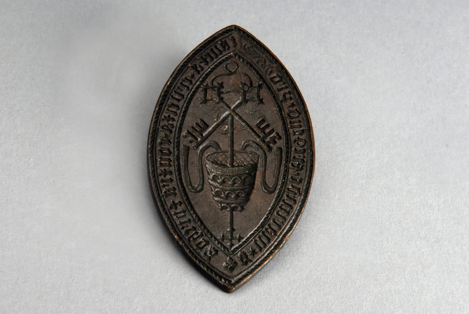 A mandorla-shaped metal disc, engraved with the reverse image of a Pope's hat and two crossed keys.