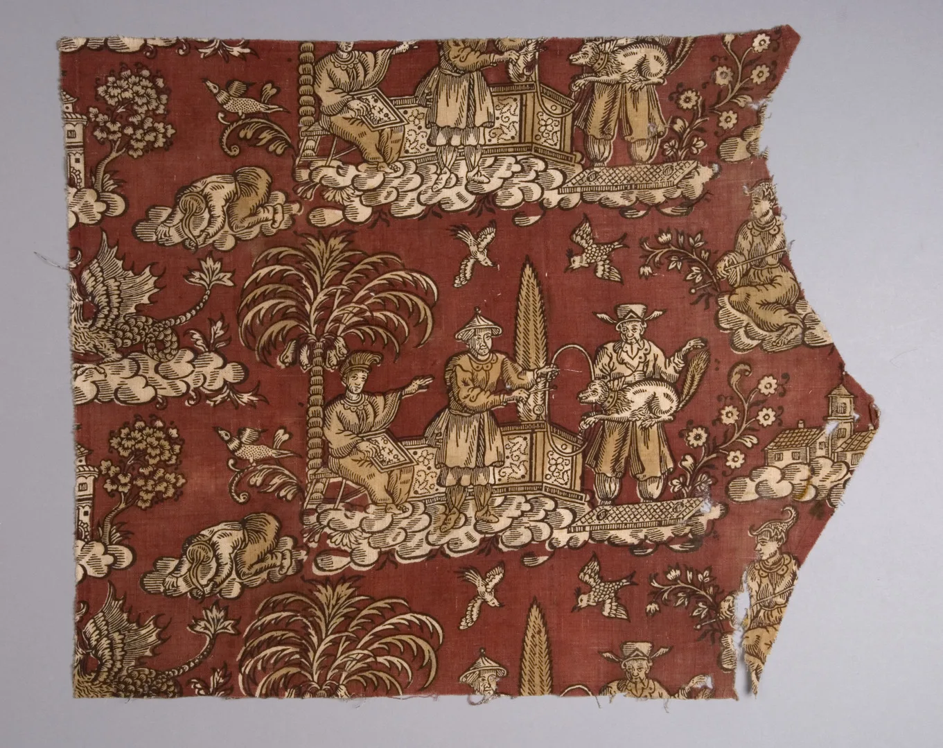 An irregular shaped piece of red fabric with yellow print depicting palmtrees, a dog and some men.