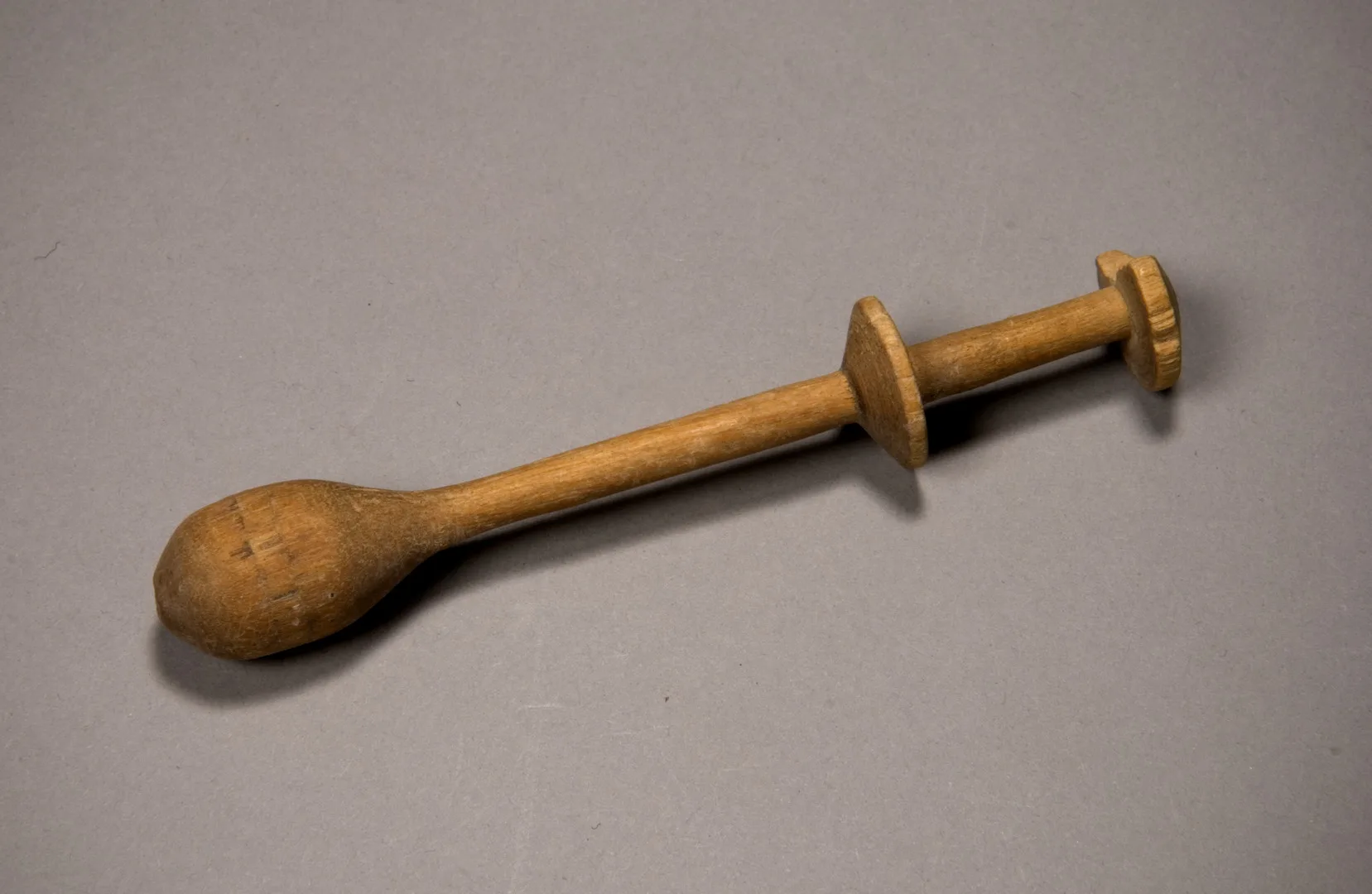 A wooden object with one thick, ball-like, end and two discs at the other end.