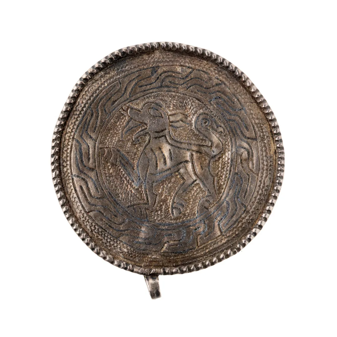 A circular, coin-like pendant with raised rim and engraved image of an animal