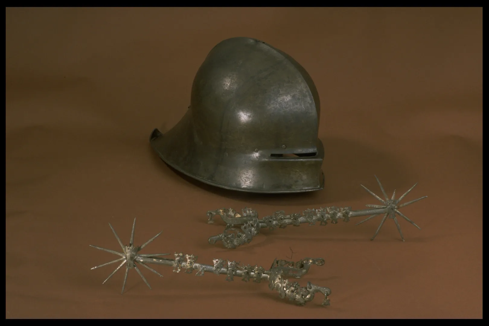 A pair of long spurs with spike wheels and a helmet with eyeslits.