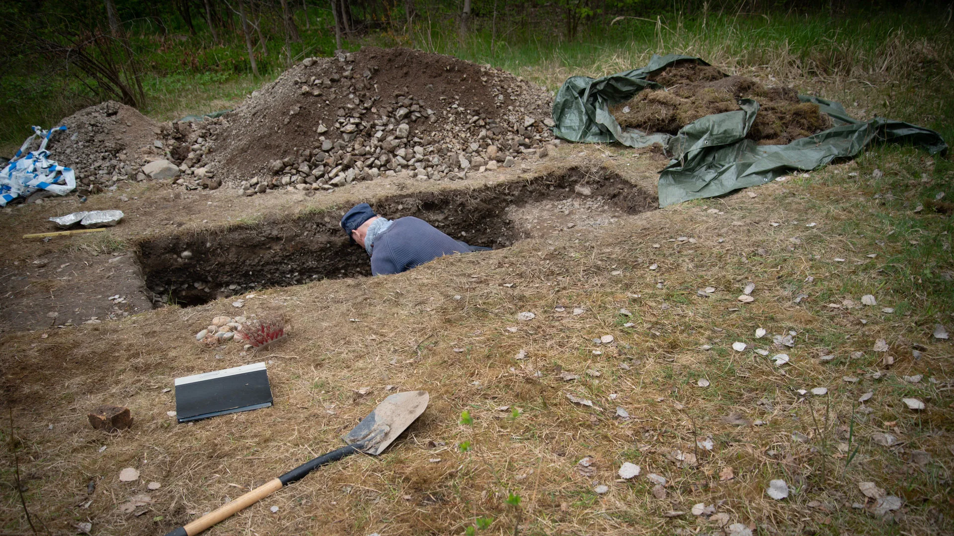 Person i en utgrävning med verktyg runt omkring