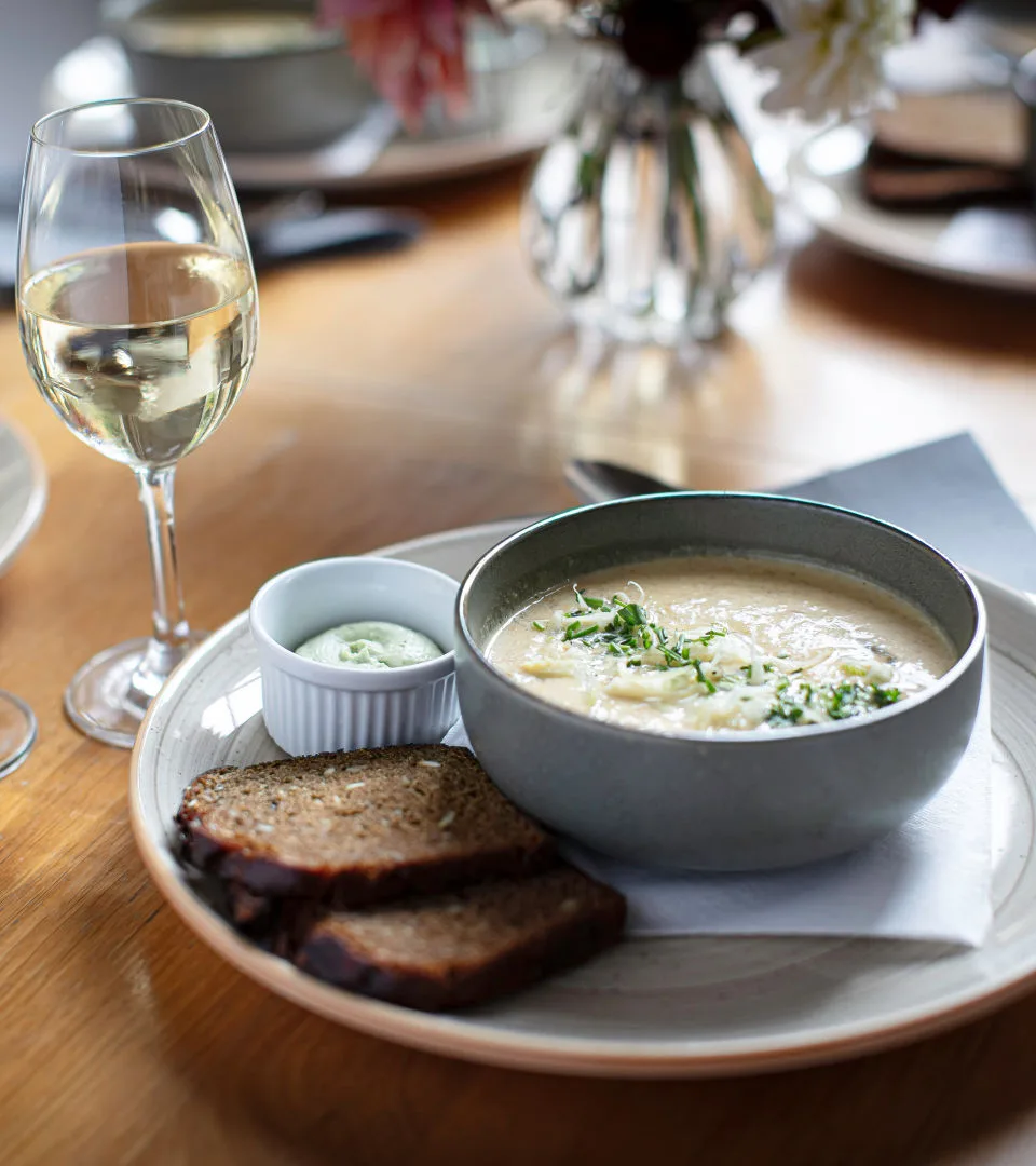 Ett glas vin. En rund tallrik med soppa. På sidan ligger två brödskivor.