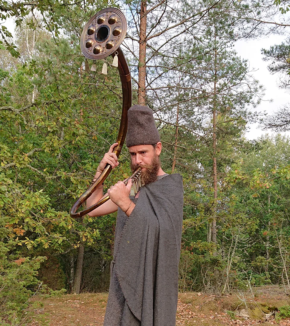 Man dressed in bronze age garment blowing in a instrumental horn