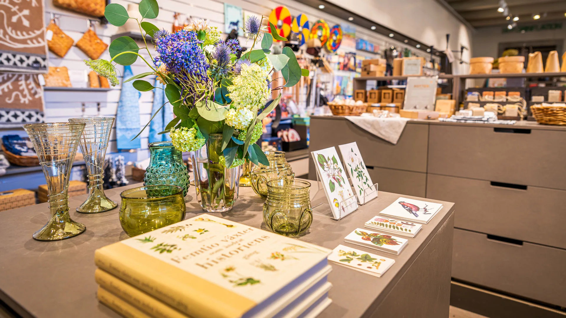Bord med varor i museibutiken. En vas med blommor.